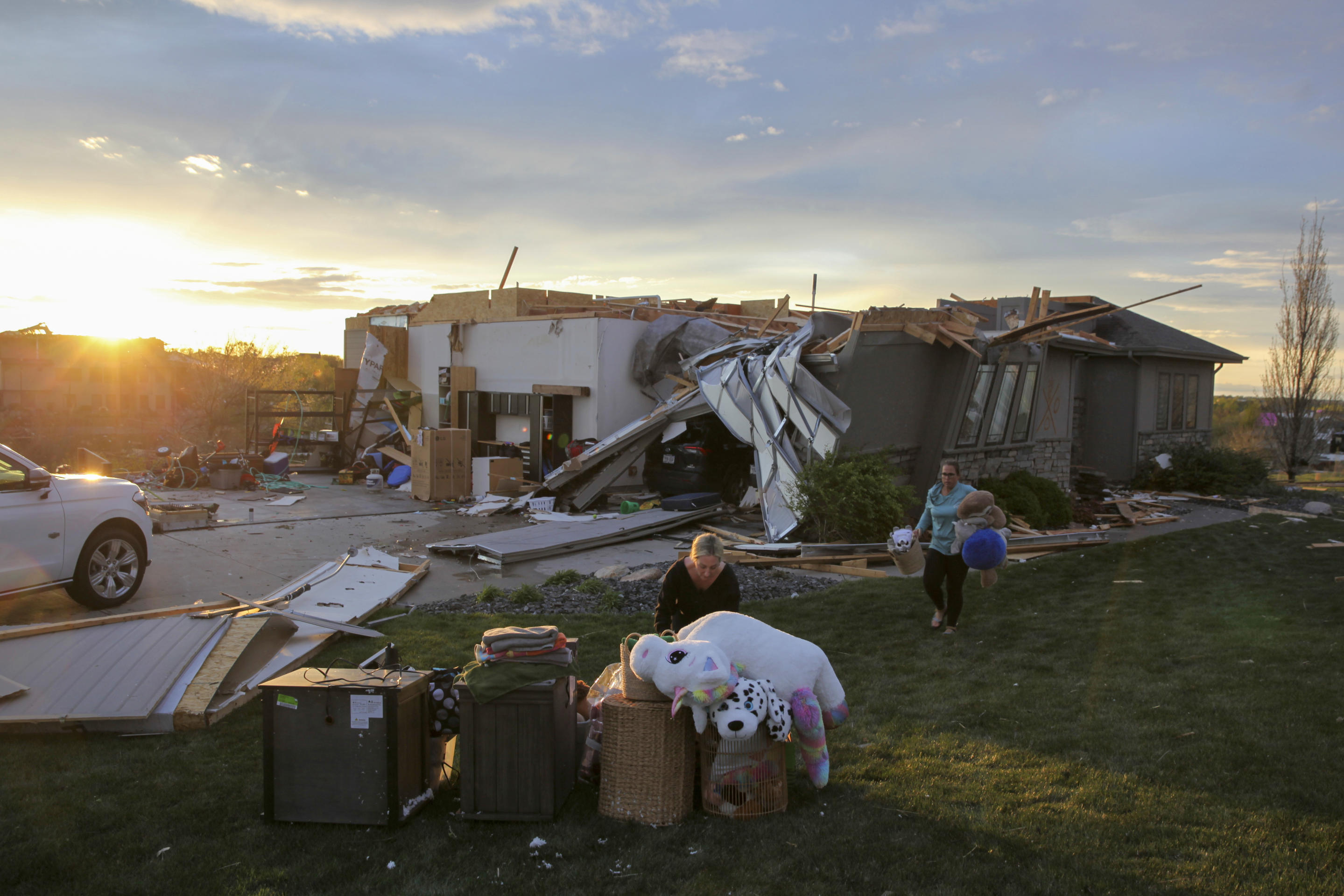 Two women help carry a friend's belongings out of their damaged home