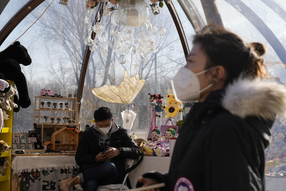 A vendor wears a mask as he waits for customers at a popup store in Beijing, Tuesday, Dec. 27, 2022. Companies welcomed China's decision to end quarantines for travelers from abroad as an important step to revive slumping business activity while Japan on Tuesday announced restrictions on visitors from the country as infections surge. (AP Photo/Ng Han Guan)