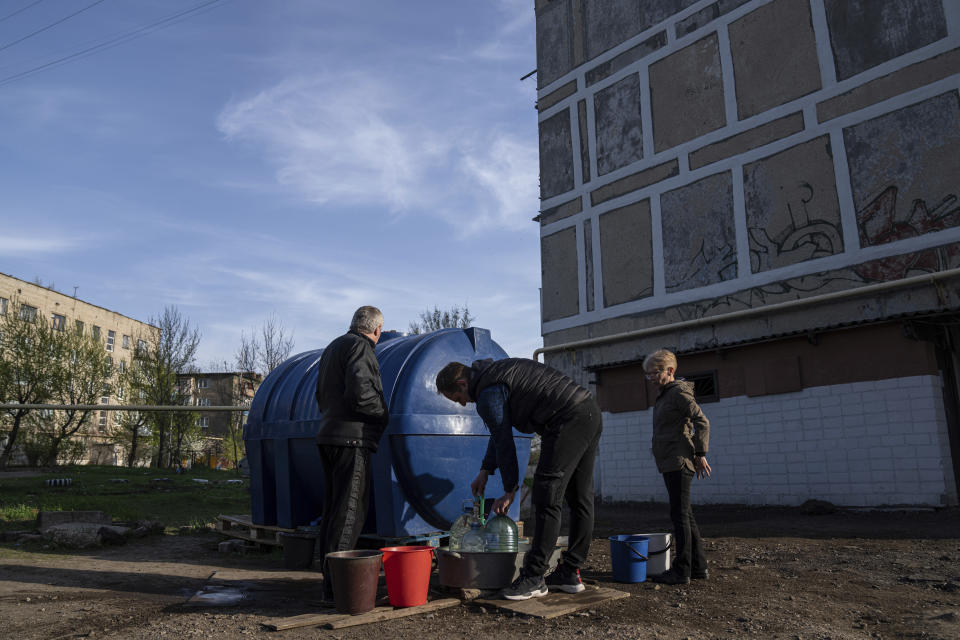 Andriy Cheremushkin, centre, fills cans with water from a water tank installed for residents of Toretsk, eastern Ukraine, Monday, April 25, 2022. Toretsk residents have had no access to water for more than two months because of the war. (AP Photo/Evgeniy Maloletka)