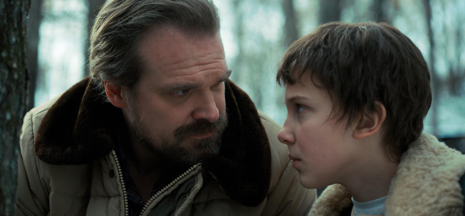 David Harbour and Millie Bobby Brown in an intense scene from a TV show, with a forest background
