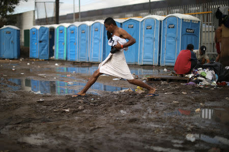 A migrant, part of a caravan of thousands from Central America trying to reach the United States, steps across mud after taking a shower at a temporary shelter in Tijuana, Mexico, November 28, 2018. REUTERS/Lucy Nicholson