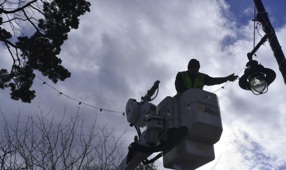 Barnstable DPW's Roger Medeiros brightens a cloudy morning as he sets out lights high above Main Street Hyannis as crews prepared the street for the annual Christmas Strol.