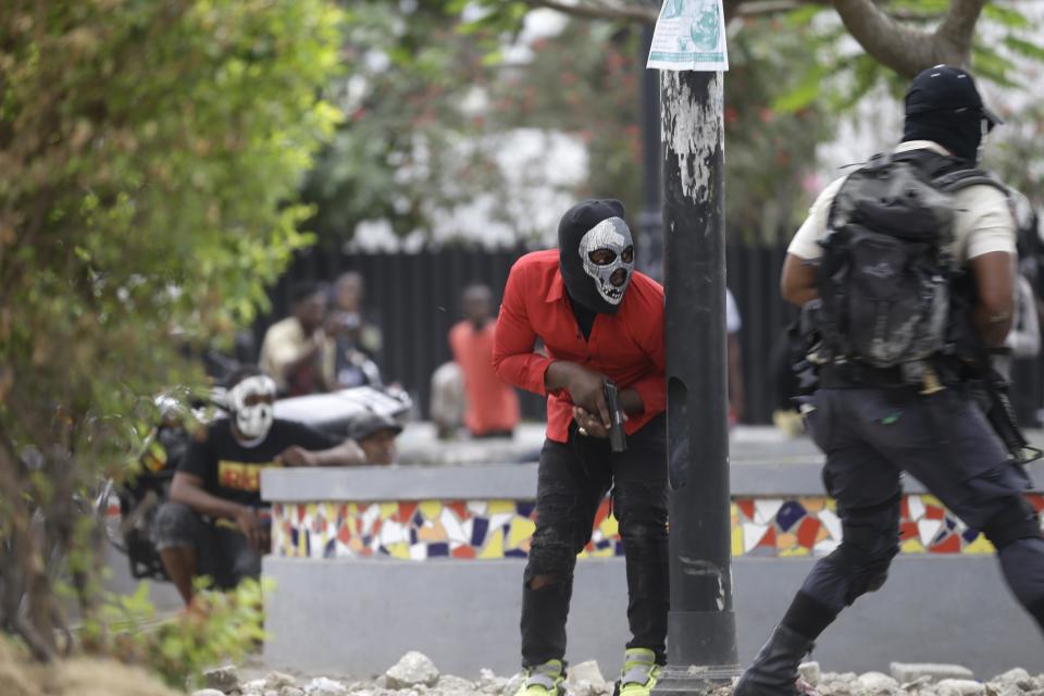 Armed off-duty police officers take cover during and exchange of gunfire with army soldiers during a protest over police pay and working conditions, in Port-au-Prince, Haiti, Sunday, Feb. 23, 2020. Off-duty police officers and their supporters exchanged fire for nearly two hours with members of the newly reconstituted Haitian army in front of the national palace. (AP Photo/Dieu Nalio Chery)