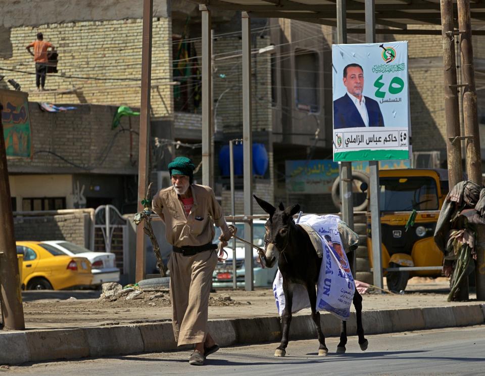 A man and his donkey pass by a campaign poster for the upcoming early parliamentary elections in Baghdad, Iraq, Monday, Sept. 20, 2021. In Iraq, electricity is a potent symbol of endemic corruption, rooted in the country’s sectarian power-sharing system. It’s perpetuated after each election cycle: Once results are tallied, politicians jockey for appointments in a flurry of negotiations based on the number of seats won. (AP Photo/Hadi Mizban)