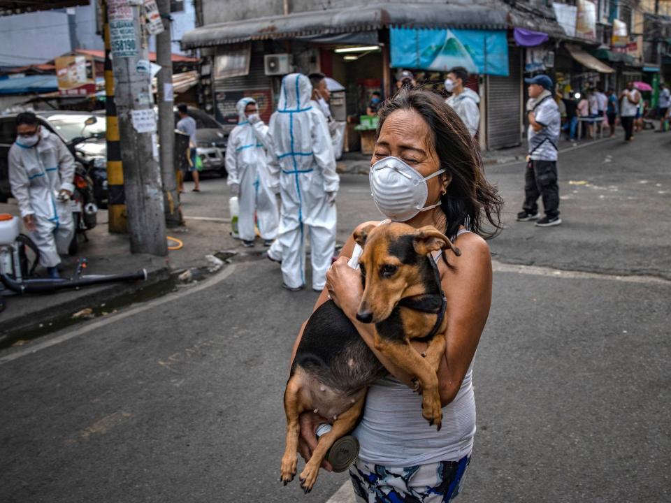 A woman wearing a face mask carries a dog as disinfection workers spray disinfectant along a street at a suburban area on March 23, Metro Manila.