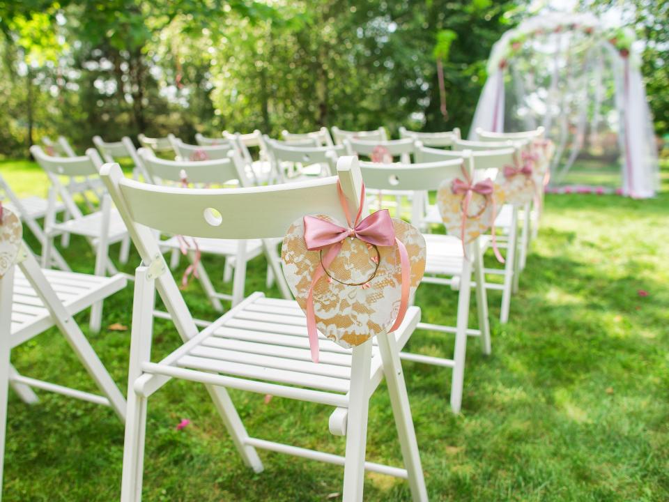 White wooden chairs at lined up on grass as seating for a wedding ceremony