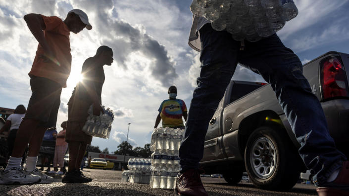 Des gens se tiennent dans un parking avec des caisses d'eau en bouteille.