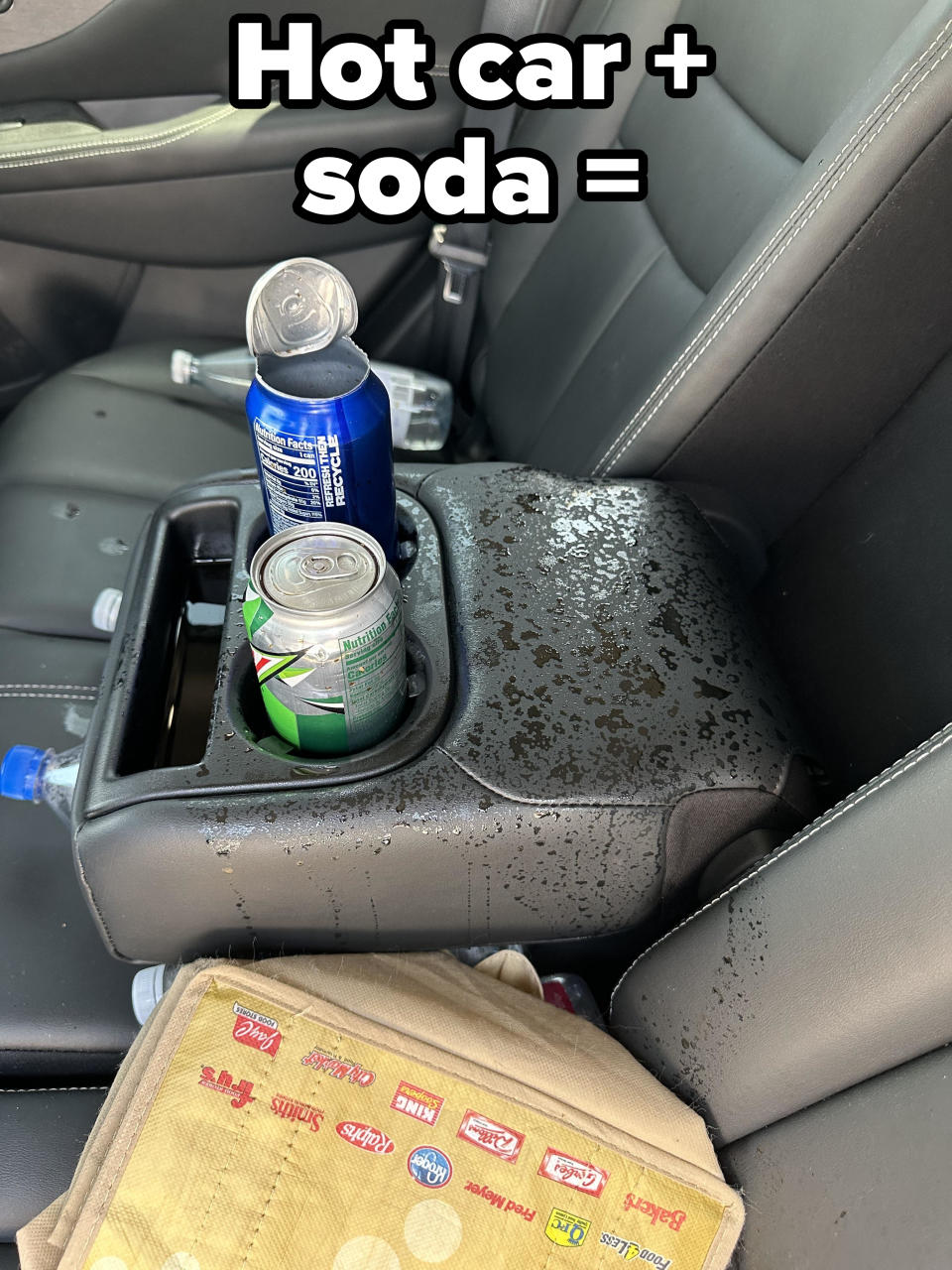 Two soda cans, one on its side and spilled onto the car's center console, with water bottles and a tote bag nearby on the backseat