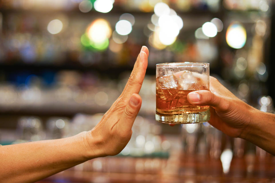 Hand refusing a glass of alcohol offered by another hand in a dimly lit bar