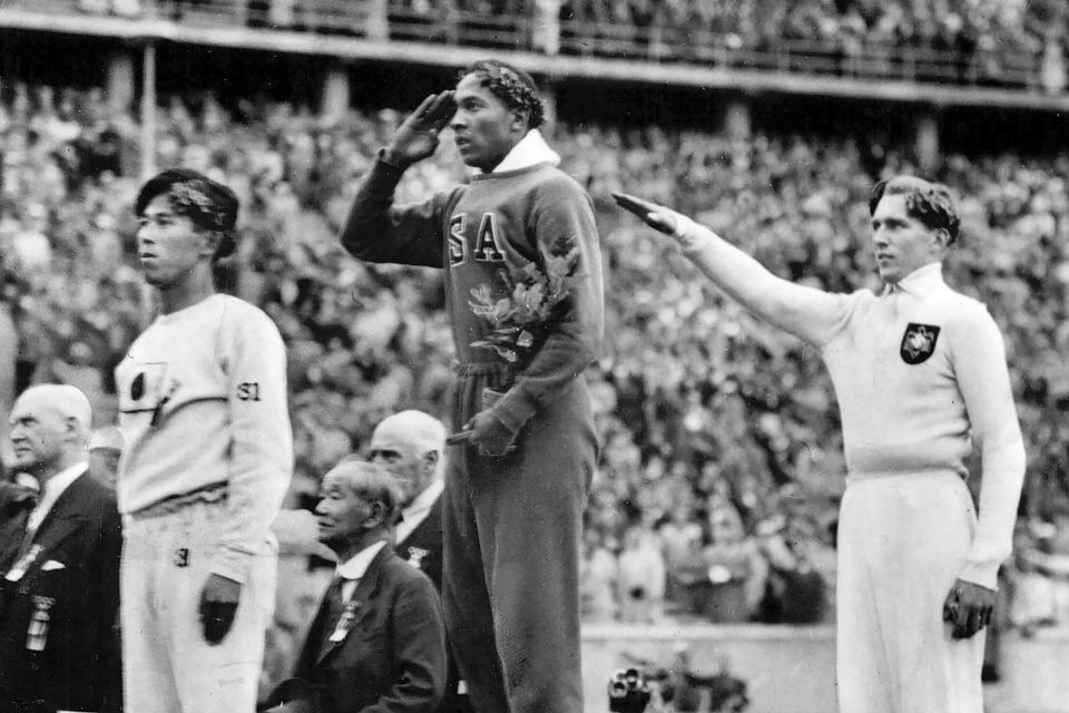 FILE - In this Aug. 11, 1936, file photo, America's Jesse Owens, center, salutes during the presentation of his gold medal for the long jump, alongside silver medalist Luz Long, right, of Germany, and bronze medalist Naoto Tajima, of Japan, during the 1936 Summer Olympics in Berlin. Scars of World War II and relics from its Nazi past are preserved at Berlin's Olympiastadion. When Spain plays England in the European Championship final, they will be playing in a stadium that doesn't hide it was built by the Nazis for the 1936 Olympic Games. (AP Photo/File)