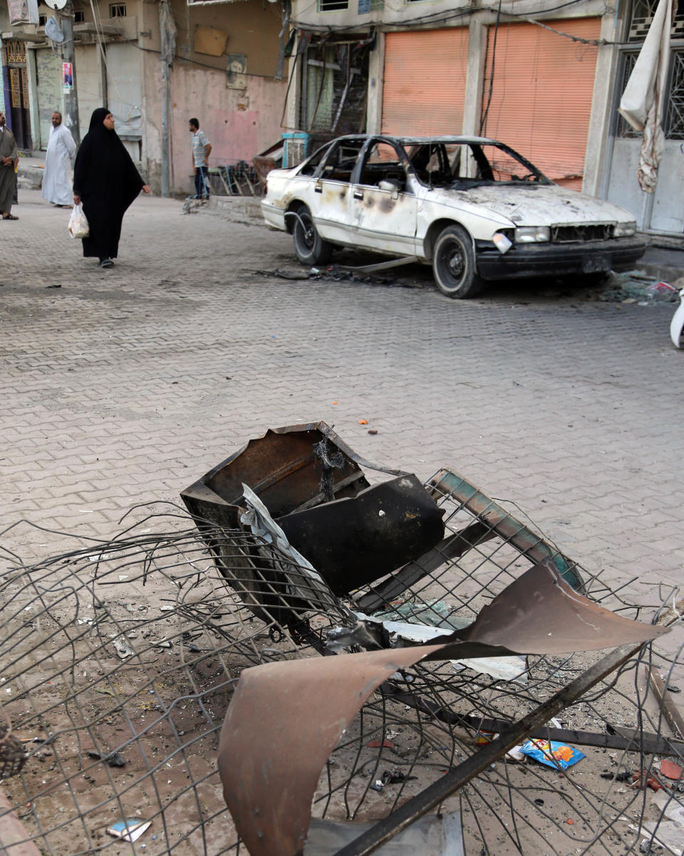 Civilians walk past damage in the aftermath of a car bomb attack in a crowded commercial street in Baghdad's eastern neighborhood of Sadr City, Iraq, Tuesday, April 22, 2014. Suicide bombings and other attacks across Iraq killed and wounded dozens on Monday, officials said, the latest in an uptick in violence as the country counts down to crucial parliamentary elections later this month. (AP Photo/Karim Kadim)