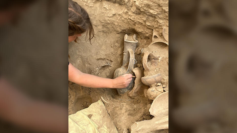 A female researcher reaches for a jug buried in the earth.