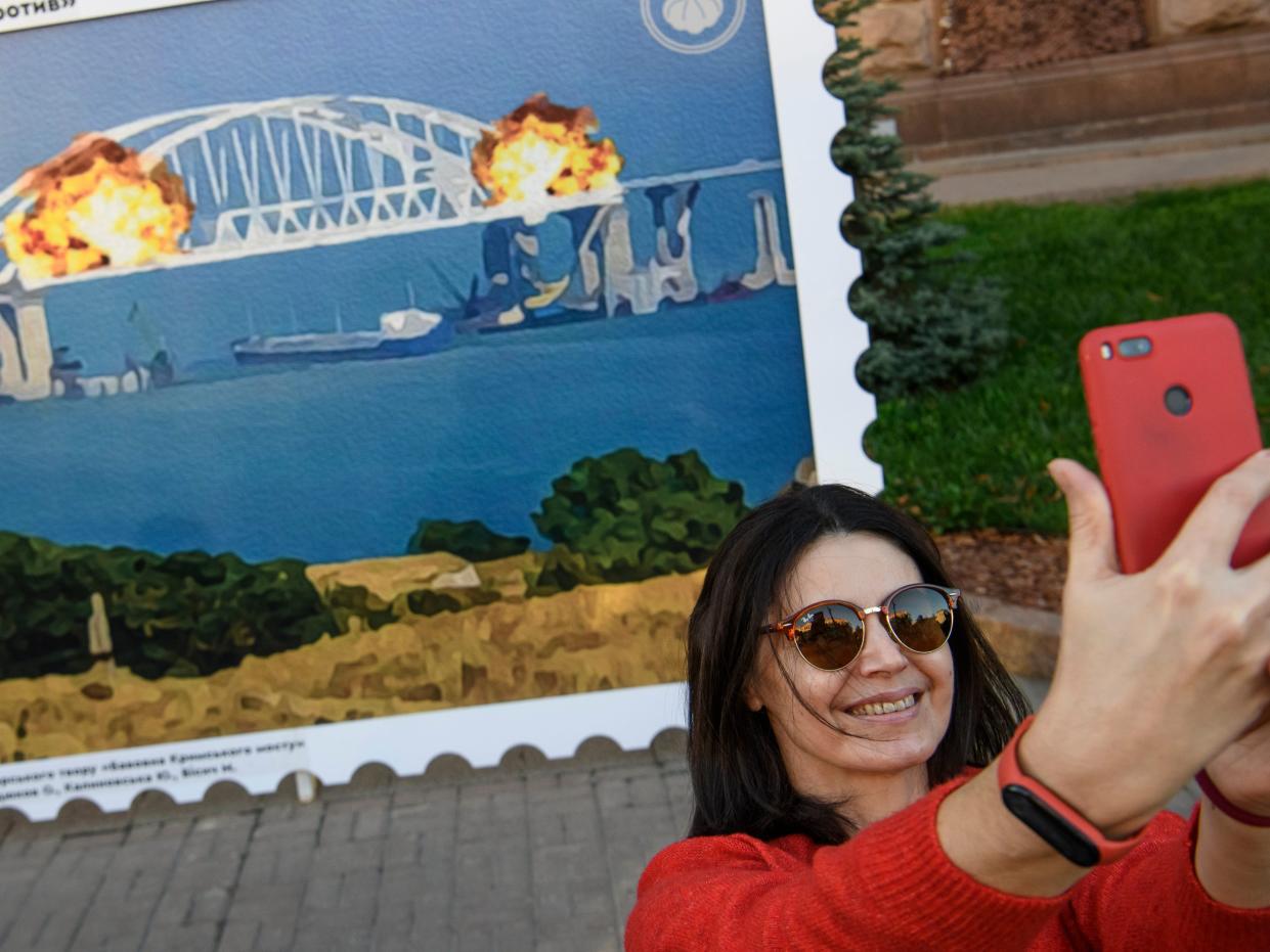 People pose for photos and take selfies in front of the large poster form of postage stamp depicting the Crimean Kerch Bridge on fire in Kyiv, Ukraine, October 08, 2022.