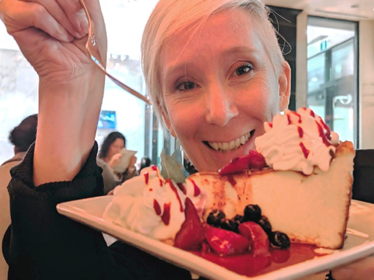 Aefa Mulholland with a slice of cheesecake covered in berries and whipped cream at the cheesecake factory