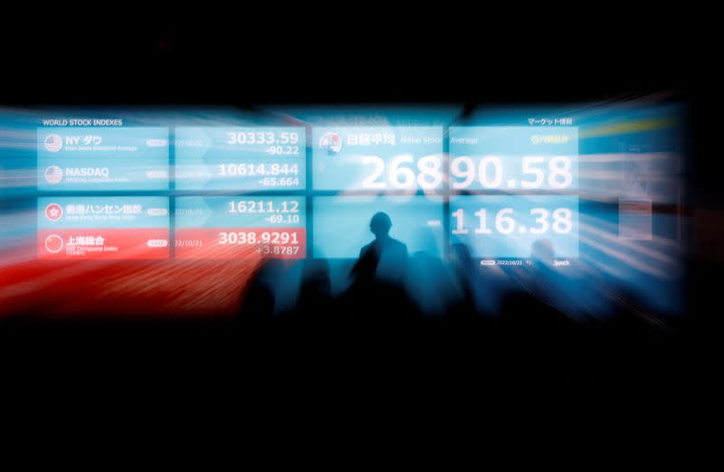 FILE PHOTO: Silhouettes of passerby are seen as they stand in front of an electric monitor displaying Japan's Nikkei share average and world stock indexes in Tokyo