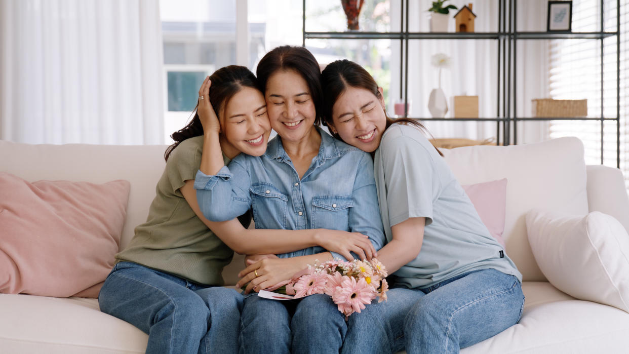 Two daughters hugging mother who has a bouquet of flowers on her lap.