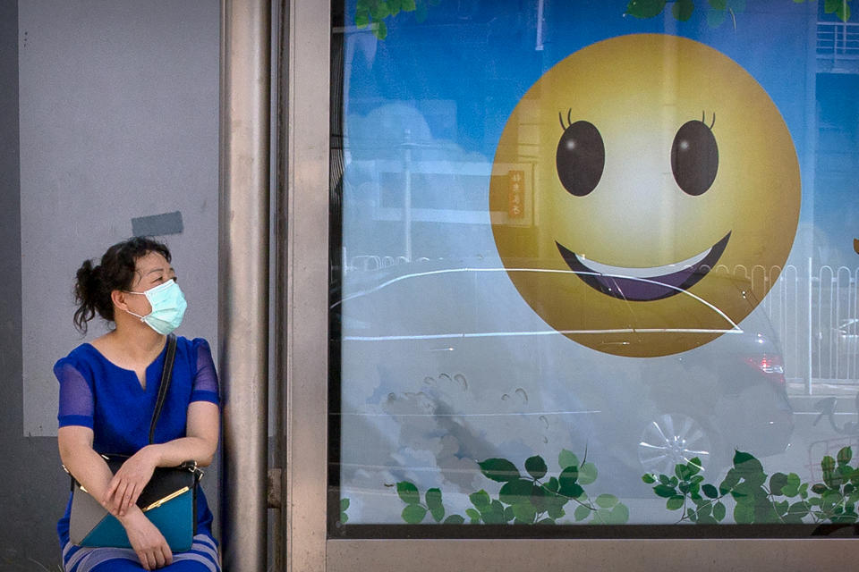 A woman wearing a face mask to protect against the new coronavirus waits at a bus stop in Beijing, Tuesday, July 14, 2020. Health experts are warning that outbreaks brought under control with shutdowns and other forms of social distancing are likely to flare again as precautions are relaxed. (AP Photo/Mark Schiefelbein)