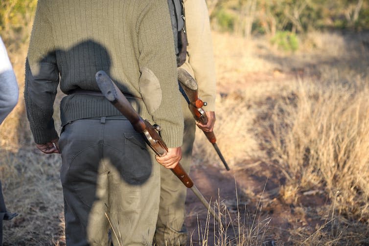 Two wildlife rangers in military-style uniforms holding rifles.