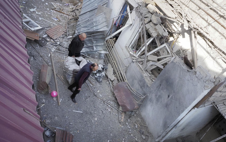 Men carry goods past a shop damaged by shelling by Azerbaijan's artillery at a market in Stepanakert, the separatist region of Nagorno-Karabakh, Saturday, Oct. 31, 2020. Nagorno-Karabakh authorities said Azerbaijani military targeted a street market in Stepanakert and residential areas of Shushi on Saturday in violation of a mutual pledge not to target residential areas made after talks in Geneva. (AP Photo)