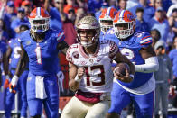 Florida State quarterback Jordan Travis (13) scrambles for yardage past Florida linebacker Brenton Cox Jr. (1) and defensive lineman Jalen Lee, right, during the first half of an NCAA college football game, Saturday, Nov. 27, 2021, in Gainesville, Fla. (AP Photo/John Raoux)