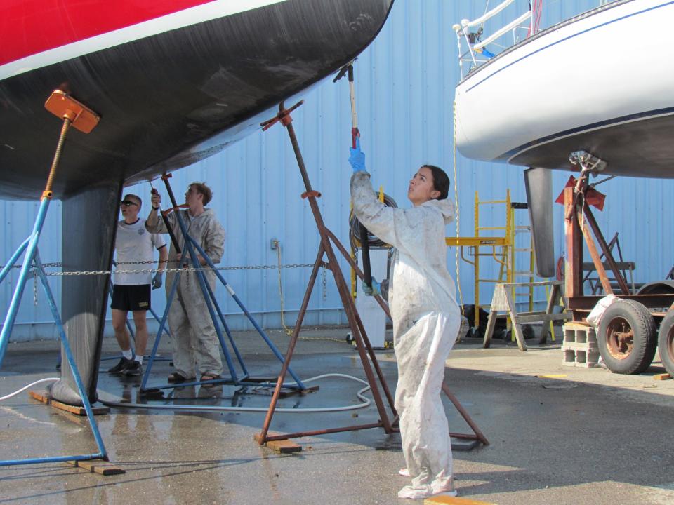 Pat Fisher, left; Elliot Brandicourt, middle; and Isabelle Navolio, right scrubbing the Avenger's hull at Desmond Marine on July 10, 2023. The Avenger crew is made up of midshipmen from the U.S Naval Academy.