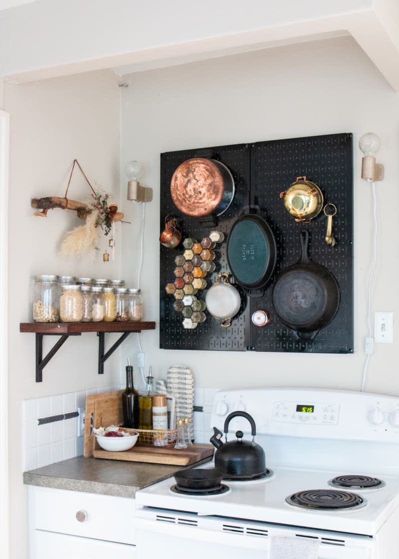 A small kitchen featuring a black pegboard above the stove that holds pots, pans, and spices