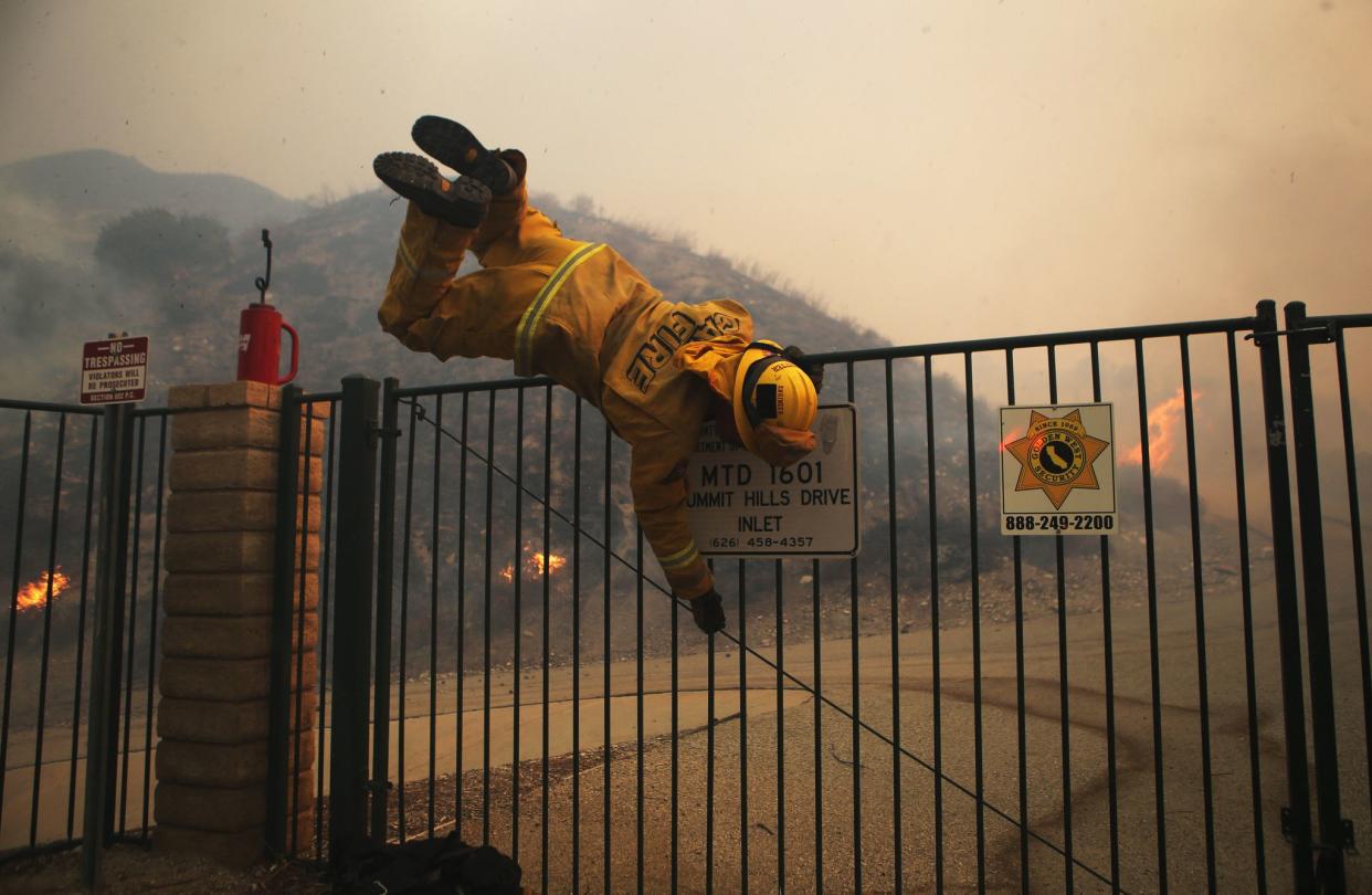 A Cal Fire firefighter hops over a locked gate while working the Tick Fire on Oct. 24, 2019 in Canyon Country, Calif.