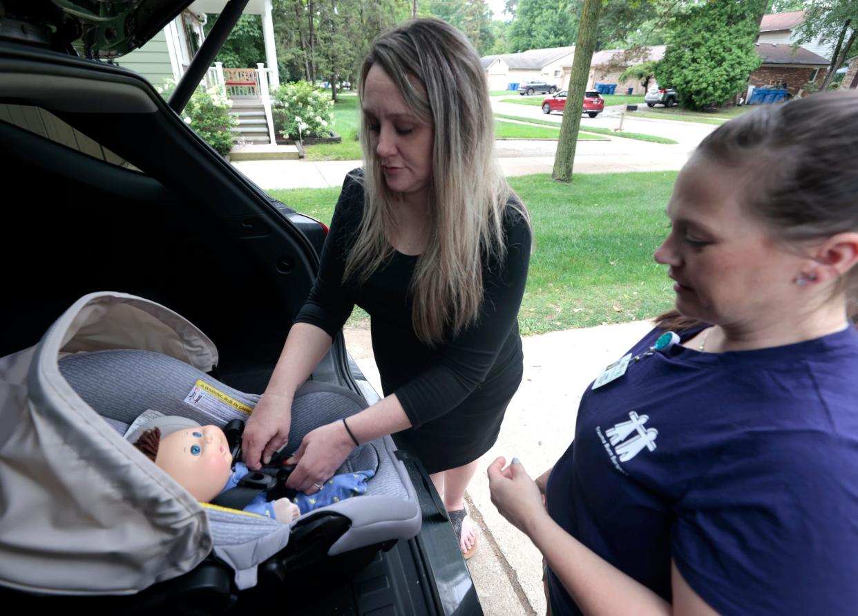 FILE -- Jessica Henson, 33, of Warren, who is 32 weeks pregnant, buckles a doll into an infant car seat as Renee Zarr, a child passenger safety technician and instructor at the Children's Hospital of Michigan, looks on at Henson's home on July 27, 2023.