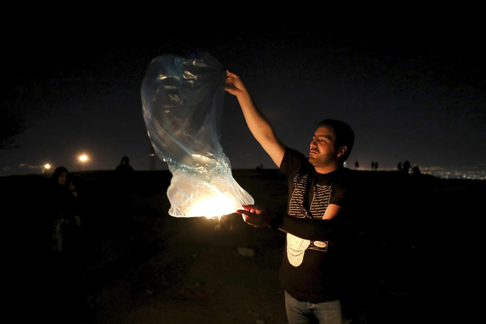 In this Tuesday, March 17, 2020 photo, an Iranian man releases a lit lantern during a celebration, known as "Chaharshanbe Souri," or Wednesday Feast, marking the eve of the last Wednesday of the solar Persian year, in Tehran, Iran. (AP Photo/Ebrahim Noroozi)