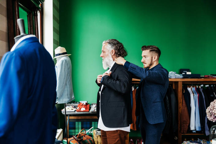 A man helping another man put on a suit.