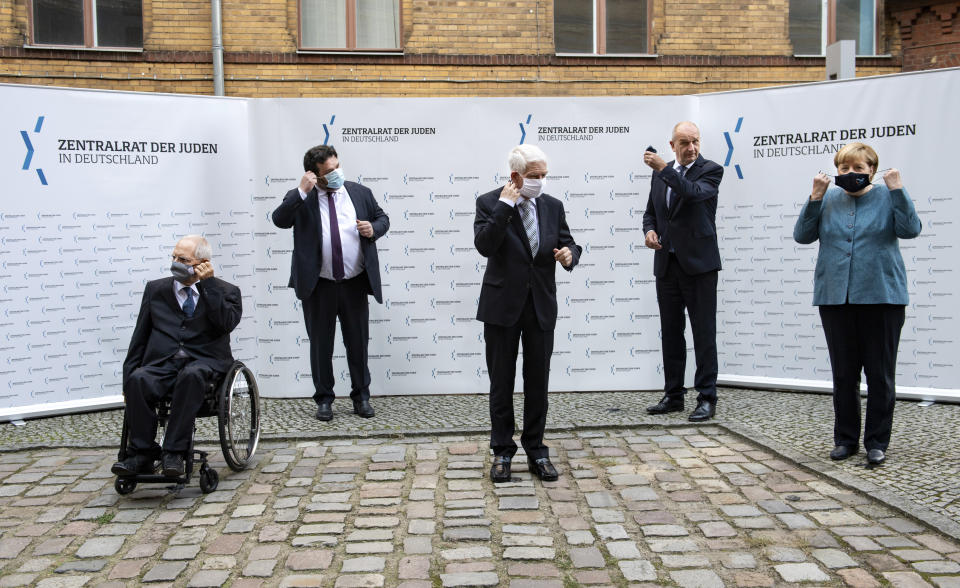 German Chancellor Angela Merkel, right, and Josef Schuster, center, President of the Central Council of Jews in Germany, joined Bundestag President Wolfgang Schaeuble, left, Gideon Joffe, second left, Chairman of the Jewish Community of Berlin, and Dietmar Woidke, second right, Minister President of Brandenburg and current President of the Bundesrat, prepare their face masks in the courtyard of the New Synagogue for a group photo at the ceremony marking the 70th anniversary of the Central Council of Jews in Berlin, Germany, Tuesday, Sept. 15, 2020. The Central Council of Jews in Germany was founded on 19 July 1950 in Frankfurt am Main. (Bernd von Jutrczenka/Pool via AP)