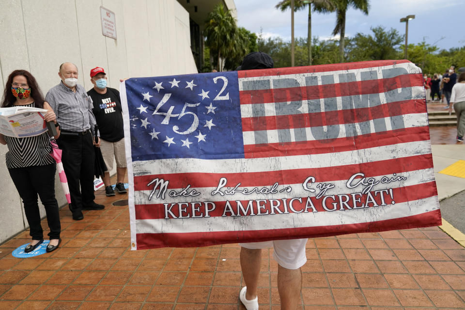 Roland Linares, 50, carries a flag in support of President Donald Trump outside of an early voting site, Monday, Oct. 19, 2020, in Miami. Florida begins in-person early voting in much of the state Monday. With its 29 electoral votes, Florida is crucial to both candidates in order to win the White House. (AP Photo/Lynne Sladky)