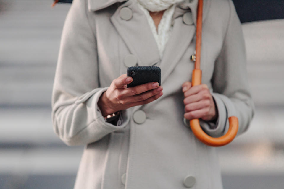 Cropped shot of an unrecognizable businesswoman texting on her cellphone while holding an umbrella outside in the rain