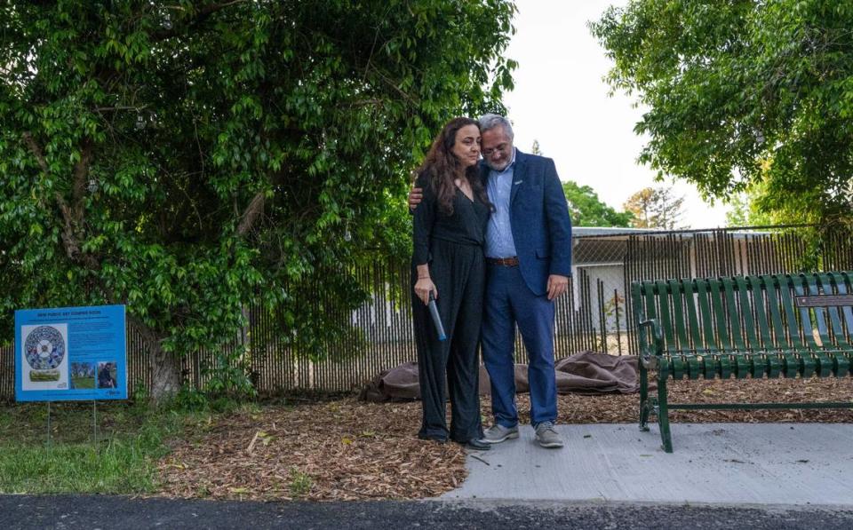 Nadine Yehya, left, and father Majdi Abou Najm stand on Monday near a bench at Sycamore Park in Davis that memorializes their son Karim Abou Najm, a UC Davis student who was fatally stabbed one year ago, during a “day of remembrance” of the event. At left, a sign depicts a sculpture that will be installed at the location in his memory.