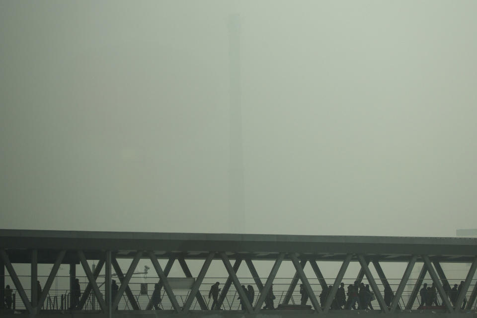 A chimney of a heating plant is obscured by heavy haze as commuters walk through a bridge linking a subway station and a bus station on a severely polluted day in Beijing Tuesday, Feb. 25, 2014. Beijing remained cloaked in hazardous white pollution hiding much of its skyline Tuesday. (AP Photo/Alexander F. Yuan)