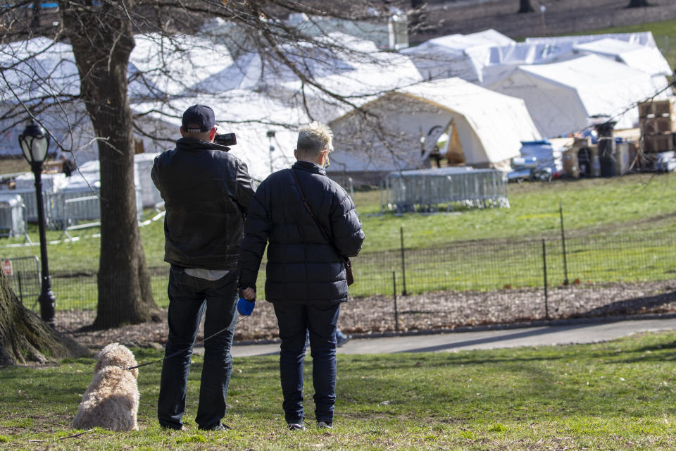 FILE- In this April 1, 2020 file photo, a couple pauses to take a picture of the Samaritan's Purse field hospital as they walk their dog in New York's Central Park. On Saturday, May 2, 2020, the Mount Sinai Hospital Health System said that it will take down the small field hospital it erected in Central Park through a partnership with a charity run by Christian evangelical preacher Franklin Graham. Only eight patients remained at the makeshift hospital as of Saturday. (AP Photo/Mary Altaffer, File)