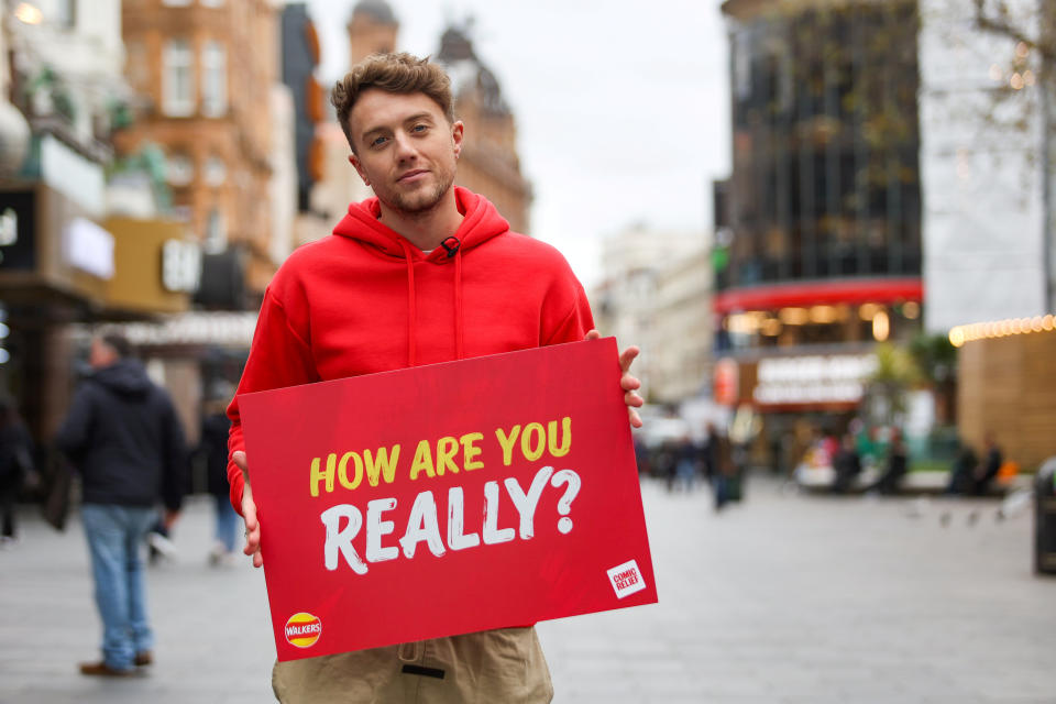 Roman Kemp holding up a sign saying 'How are you really?' (SWNS)