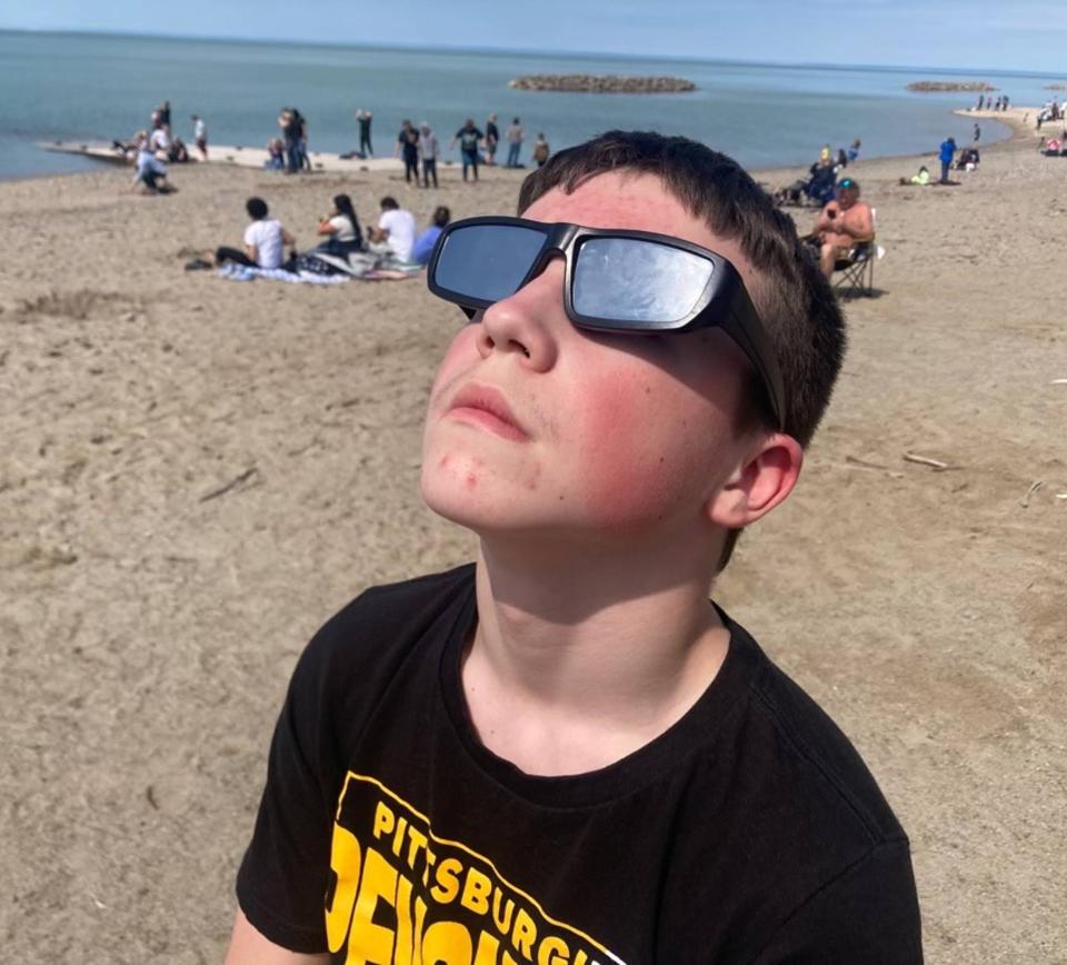 Matthew Campbell, 12, of Canonsburg, looks at the sun through his eclipse glasses at 2:15 on Presque Isle's Beach 1 on Monday.