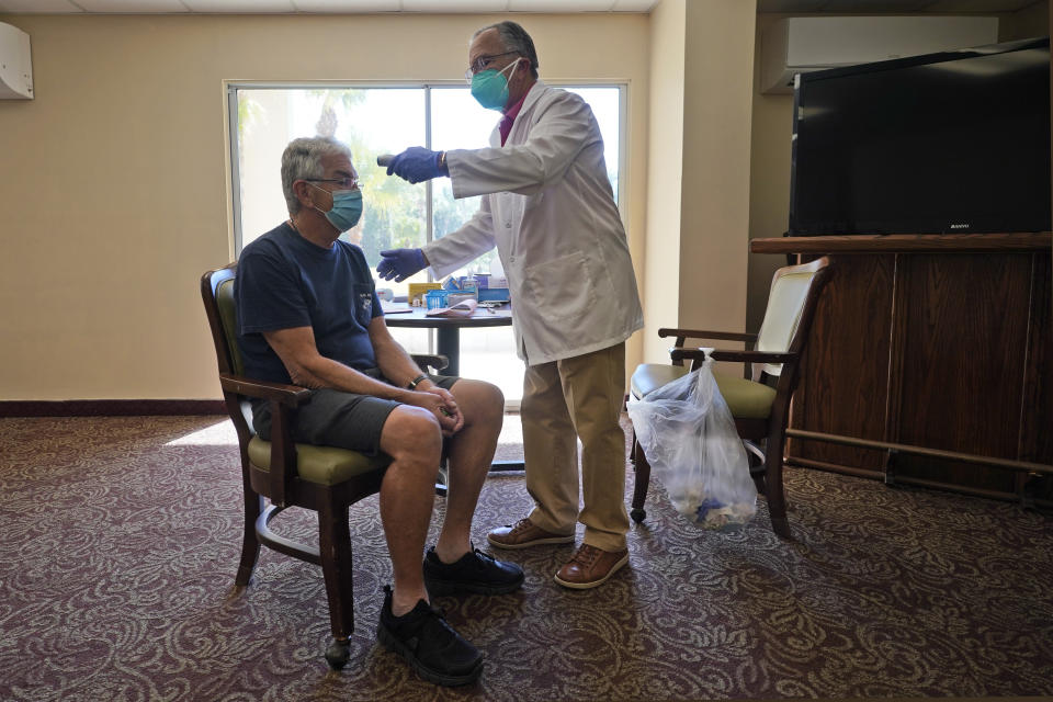 Registered Pharmacist Ken Ramey, right, takes the temperature of William M. Derrick, 77, before administering the COVID-19 vaccine, Thursday, Jan. 21, 2021, at the Isles of Vero Beach assisted and independent senior living community in Vero Beach, Fla. (AP Photo/Wilfredo Lee)