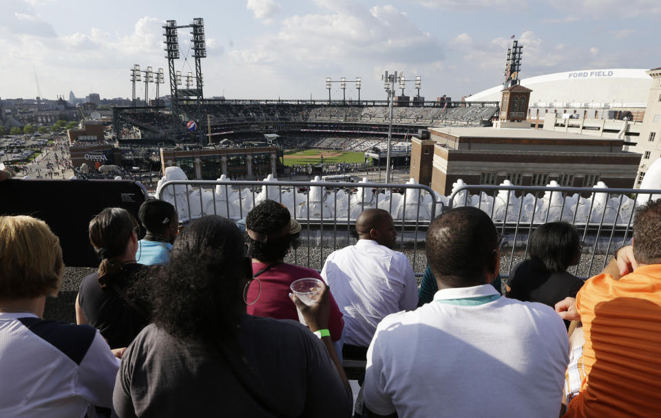 FILE - In this July 12, 2013, file photo, baseball fans watch from the roof of the Detroit Opera House before a baseball game between the Detroit Tigers and the Texas Rangers in Detroit. This week, Major League Baseball players and owners reached an agreement to play an abbreviated, 60-game season that would start July 23 or 24 in teams’ home ballparks. But the seats will be empty. Instead, fans hoping to see a game in person will be have to settle for pressing their faces up against hotel windows, squinting through metal grates or climb to rooftops when baseball returns this month in otherwise empty stadiums. (AP Photo/Carlos Osorio, File)