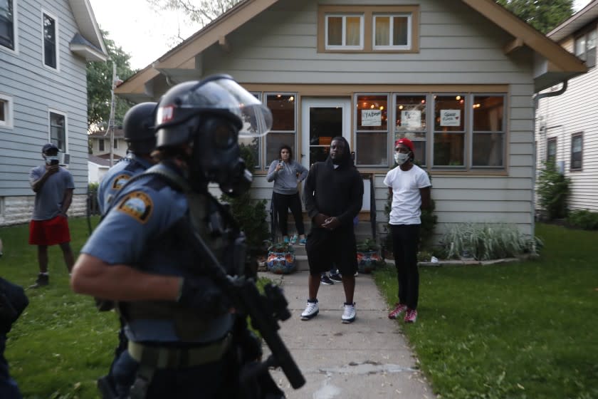 Bystanders watch as police walk down a street Thursday, May 28, 2020, in St. Paul, Minn. Protests over the death of George Floyd, a black man who died in police custody, broke out in Minneapolis for a third straight night. (AP Photo/John Minchillo)