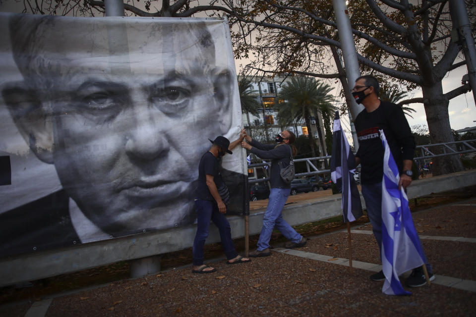 ARCHIVO - En esta foto del 25 de abril del 2020, manifestantes con mascarillas protectoras cuelgan un cartel con la imagen del primer ministro israelí Benjamin Netanyahu en una protesta contra Netanyahu y la corrupción gubernamental en la Plaza Rabin, en Tel Aviv. (AP Foto/Oded Balilty)