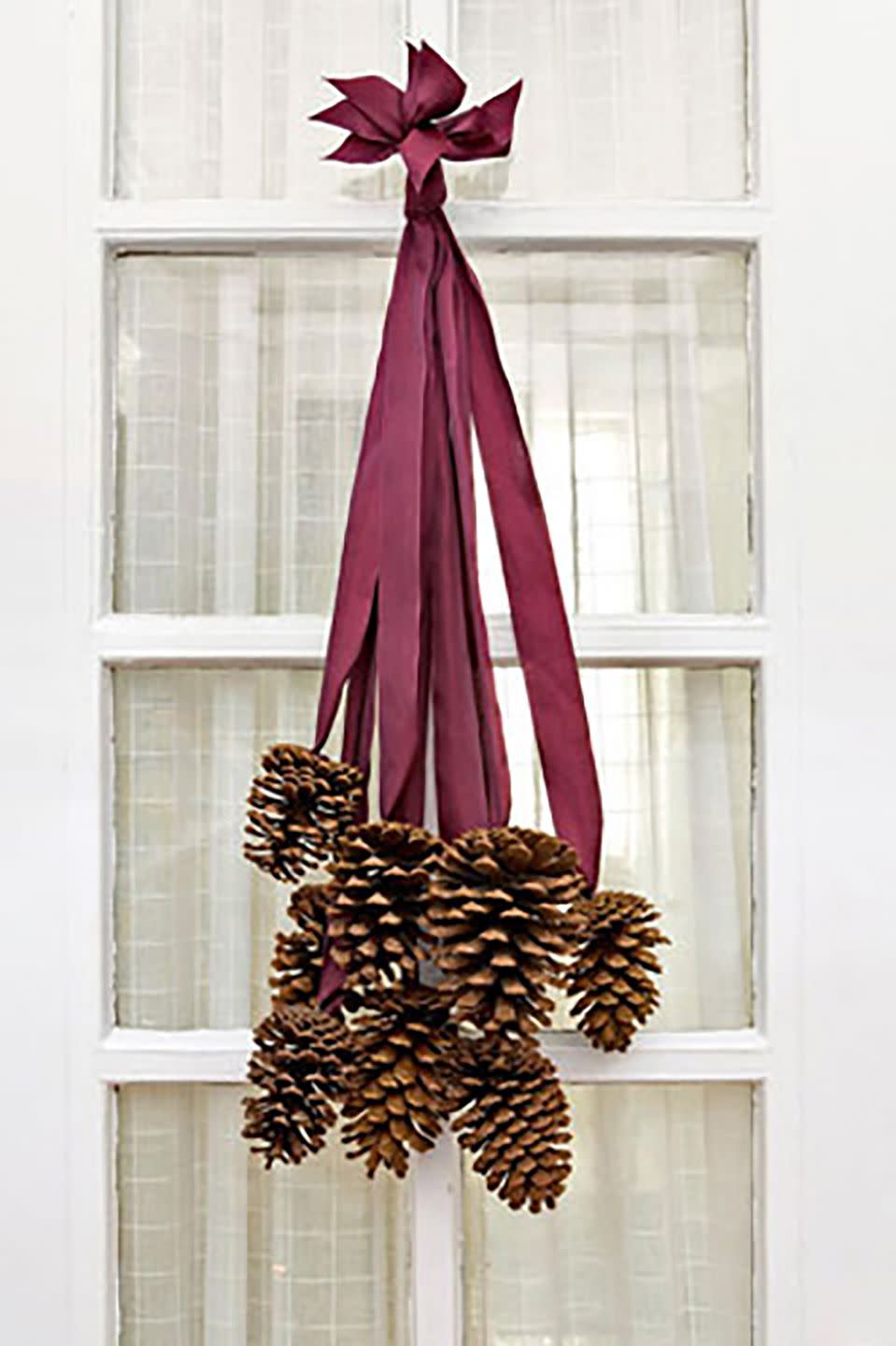 <p>Not all DIY front-door decor requires a foam wreath form. To make this elegant cluster, we selected 8 four- to six-inch pinecones and 8 two-foot-long pieces of silk ribbon. Use a hot-glue gun to adhere the last two inches of each ribbon to the base of a cone. After the glue dries, collect all the ribbon ends and stagger them so that the cones fall at varying lengths. Tie the ribbon ends together in a knot, trim the tips so they are uniform, and slip the knot over a finishing nail. </p>