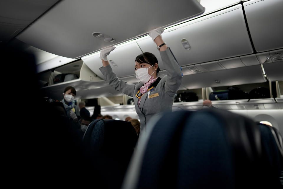 A flight attendant closes the overhead compartment on a flight to Tokyo from Frankfurt, Germany, Sunday, July 18, 2021. (AP Photo/Natacha Pisarenko)