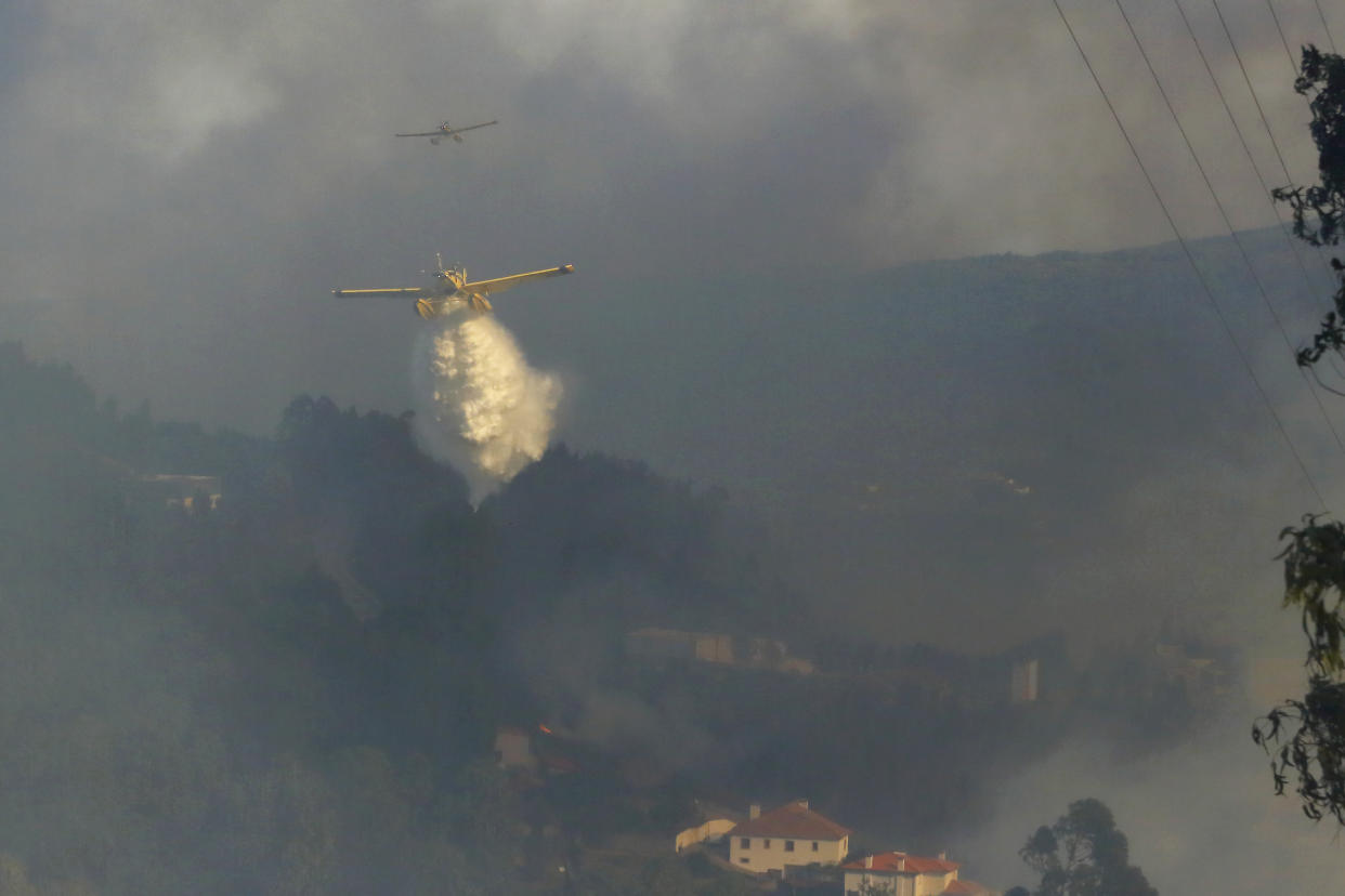 Firefighting airplanes drop water on a fire burning near houses in Sever do Vouga, a town in northern Portugal that has been surrounded by wildfires, Monday, Sept. 16, 2024. (AP Photo/Bruno Fonseca)