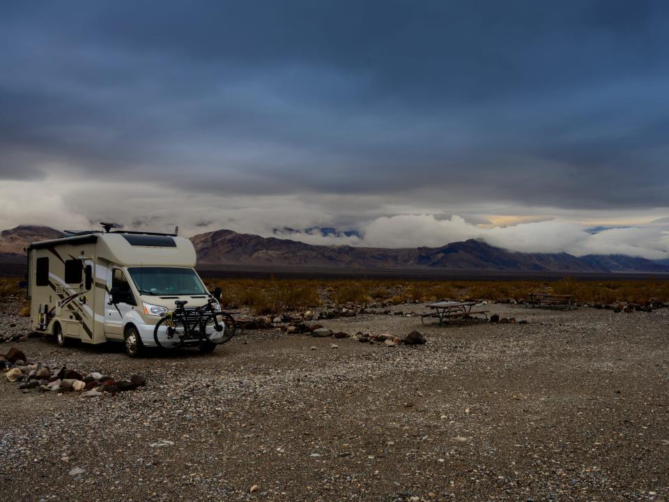 An RV is parked in  a desert valley on a dark, gloomy day.