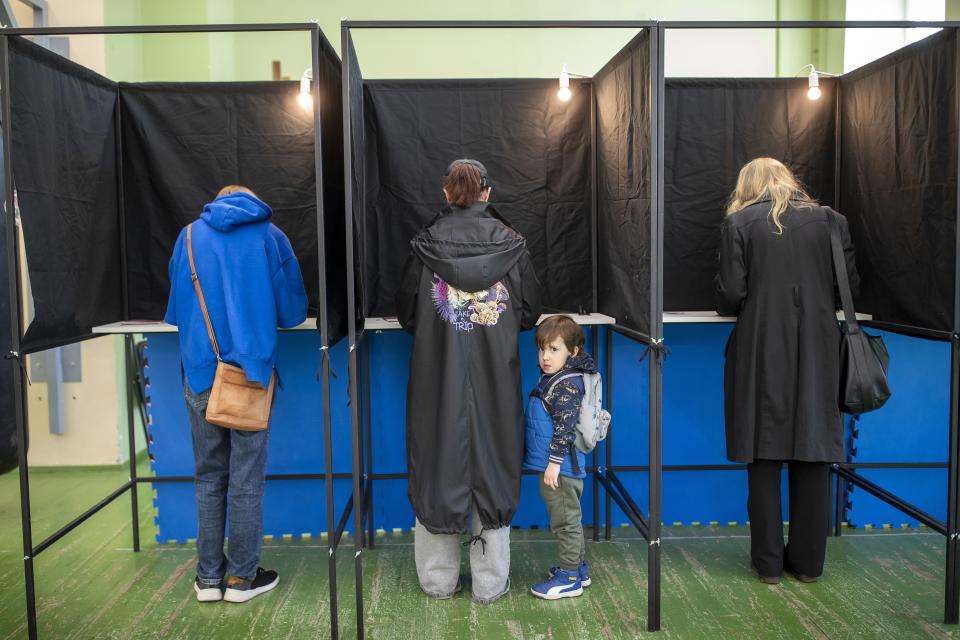 A boy looks from a voting booth as his relative fills-in a ballot at a polling station during the first round of voting in presidential elections in Vilnius, Lithuania, Sunday, May 12, 2024. (AP Photo/Mindaugas Kulbis)