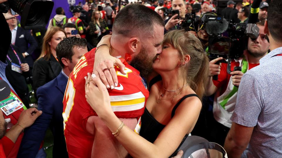 Taylor Swift and Travis Kelce kiss, surrounded by photographers