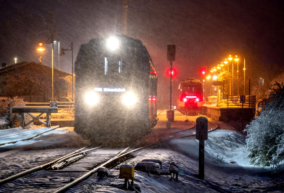 A train leaves the station in Wehrheim near Frankfurt, Germany, as snow falls early Tuesday, Nov. 28, 2023. The train to Frankfurt at right stranded because of trees blocking the rails. (AP Photo/Michael Probst)