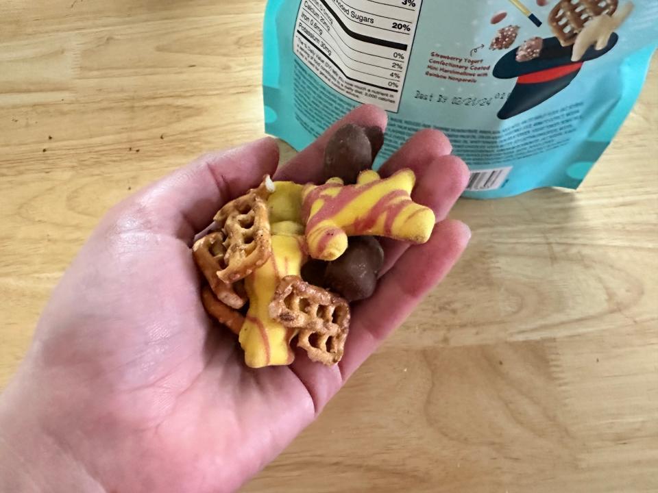 hand holding yellow and pink covered crackers, pretzels in front of table